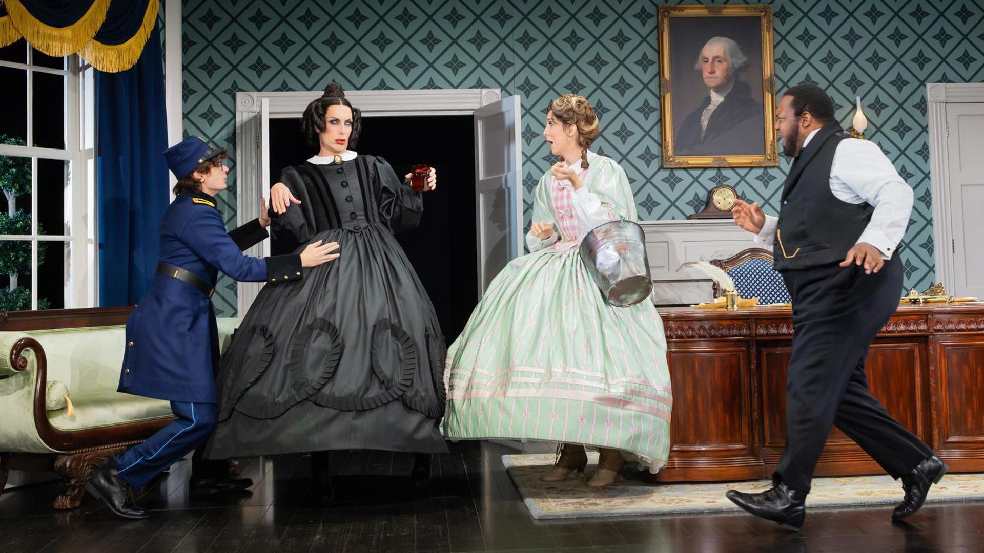 An actress in a black dress staggers unsteadily holding a red glass, three other actors rush to her to help, including an actress in a green dress holding a bucket.