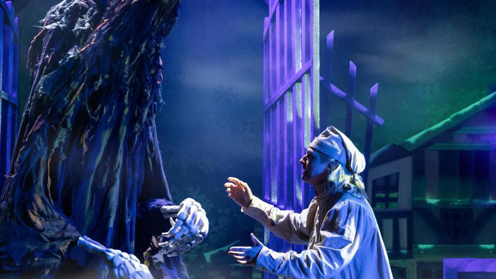 Performer gesturing to a large puppet in front of an open gate.