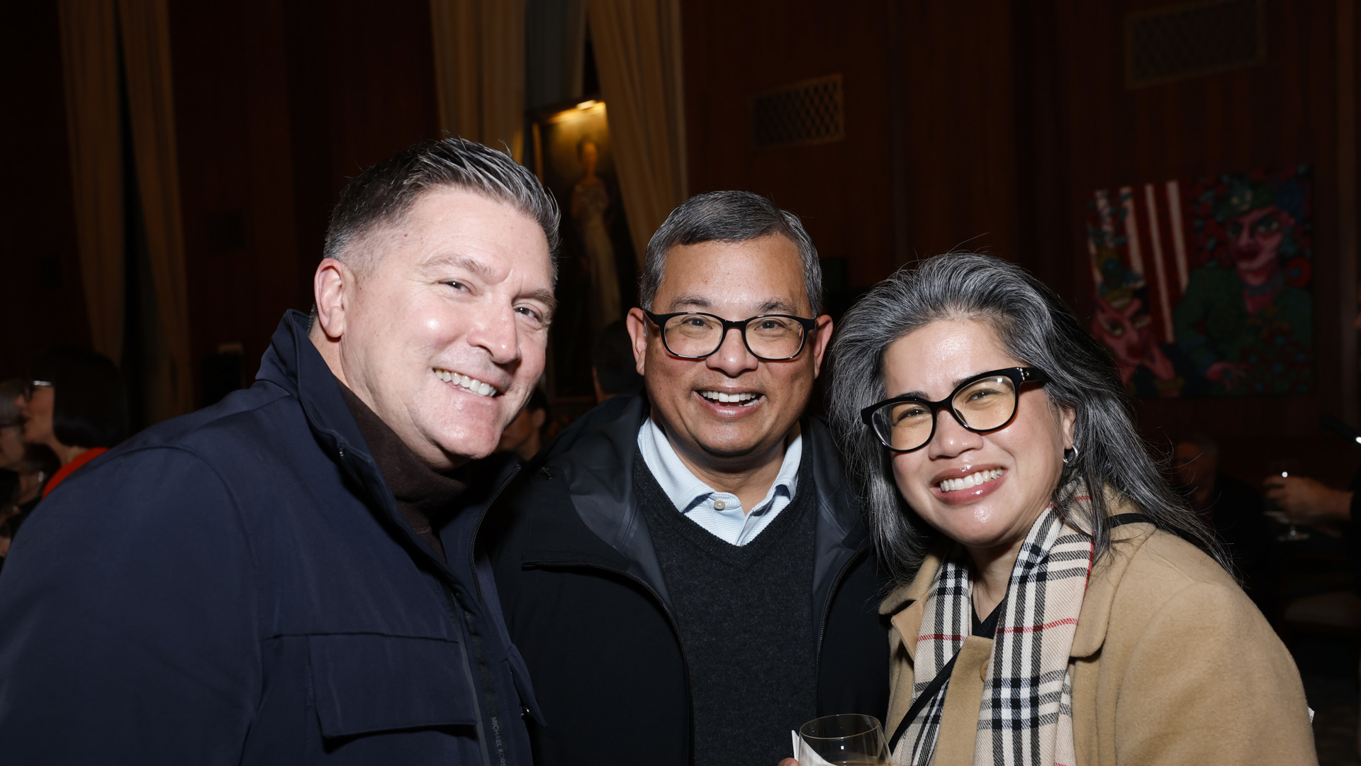 Three people gather for a photo holding wine. 