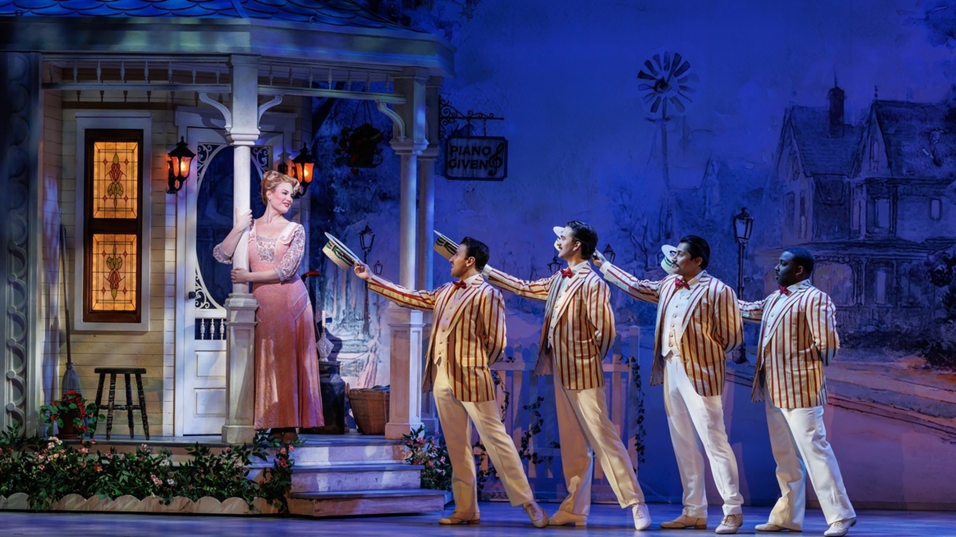 An actor stands on the porch of a house, hugging one of the poles of the porch. She looks at four men dressed in striped suit jackets who are tipping their hats to her.