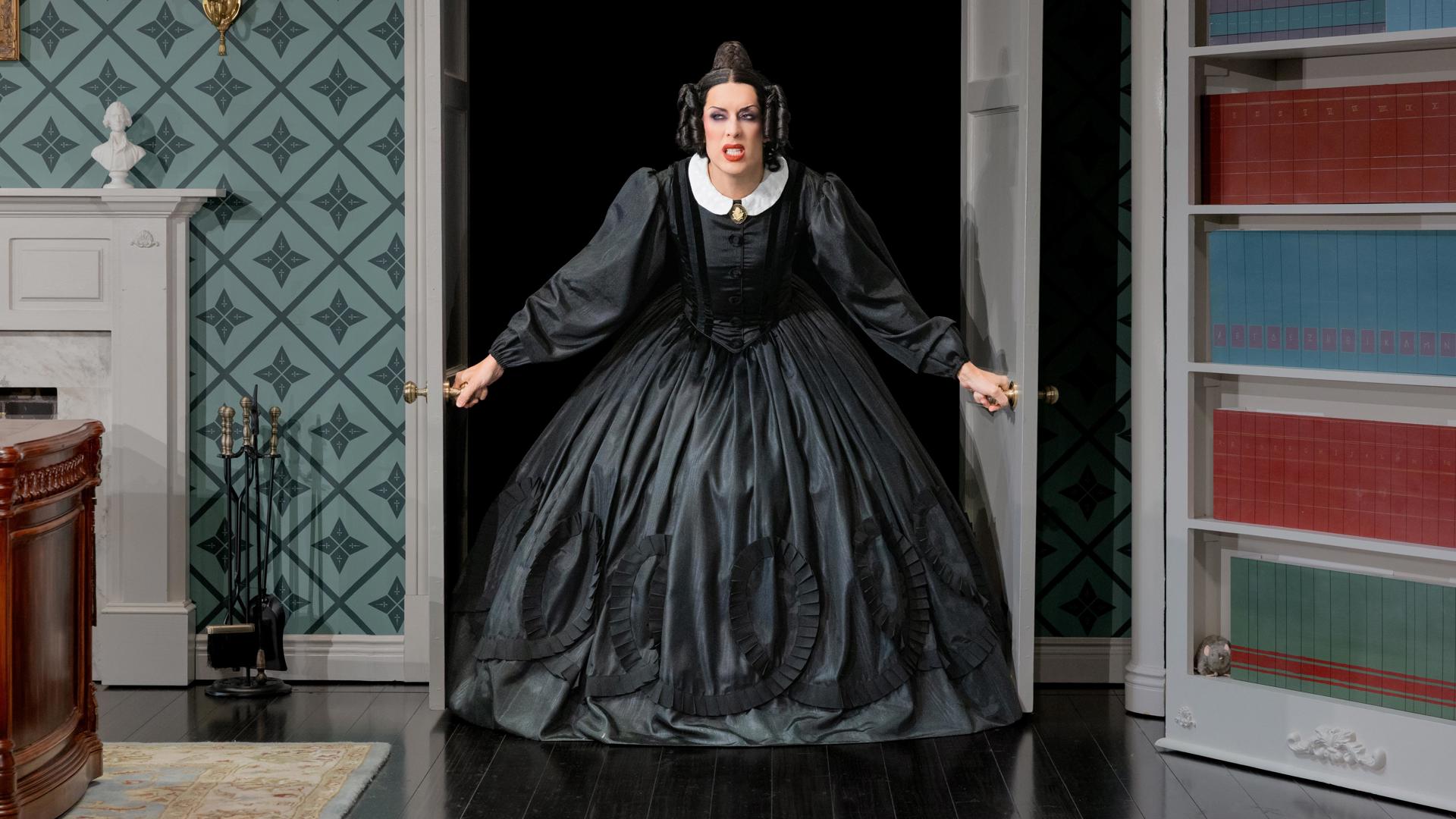 An actress in a black dress bursts through a set of double doors with a scowl on her face.